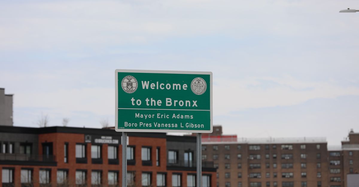 A cityscape featuring the Welcome to the Bronx sign in New York City, with residential buildings in the background.